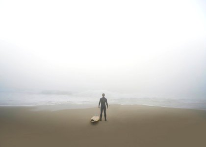 man standing beside surfboard on seashore