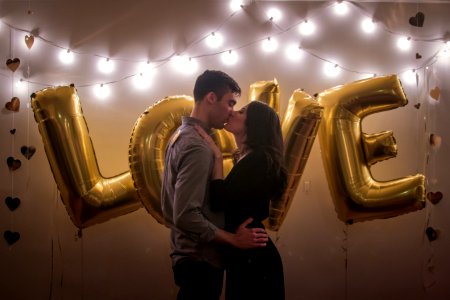 A couple kissing in front of gold colored balloons that spell out "Love." photo