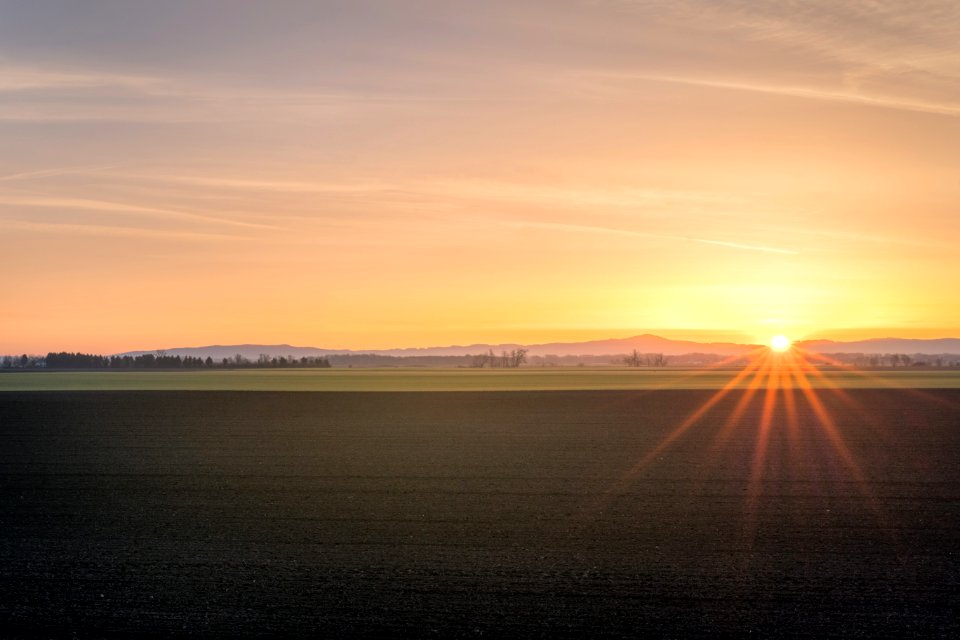 brown soil field across mountain under orange sunset sky