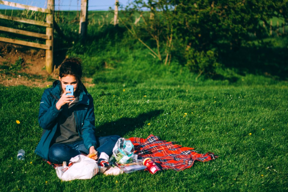 woman in blue outfit using blue smartphone while sitting on grass