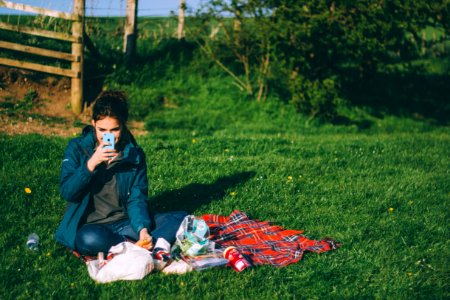 woman in blue outfit using blue smartphone while sitting on grass photo