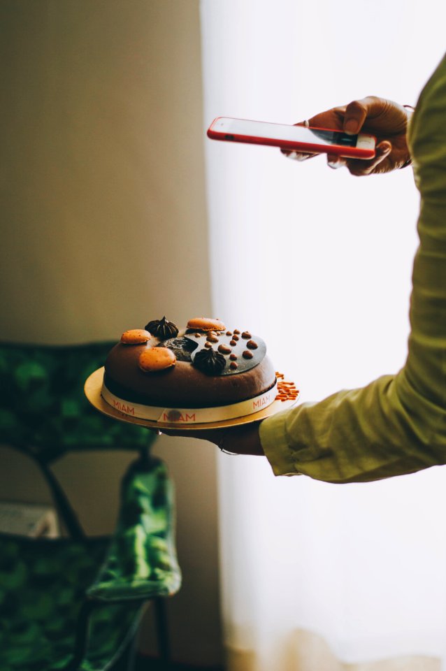 person holding iPhone taking photo of cake near curtains