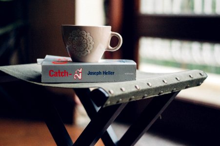 close-up photography of beige ceramic coffee cup on top of Joseph Heller book photo