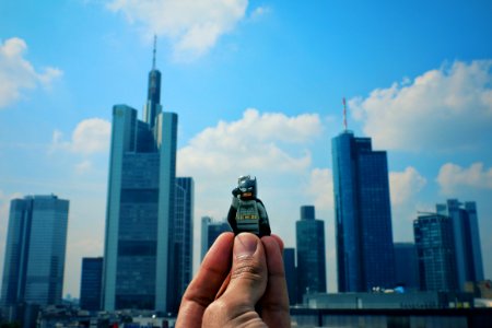 A person holding a Lego guy toy in the air with his fingers, with skyscrapers and a cloudy sky in the background. photo