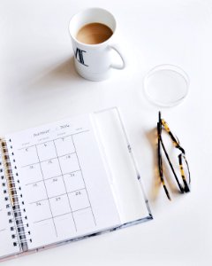 A calendar book, pair of glasses and cup of coffee on a white surface. photo
