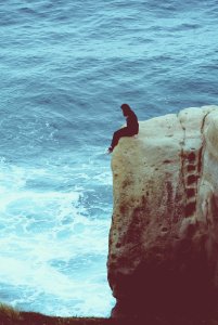 person sitting on edge of rock looking at sea photo