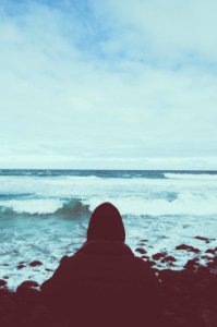person sitting on rocking shore under cloudy sky photo