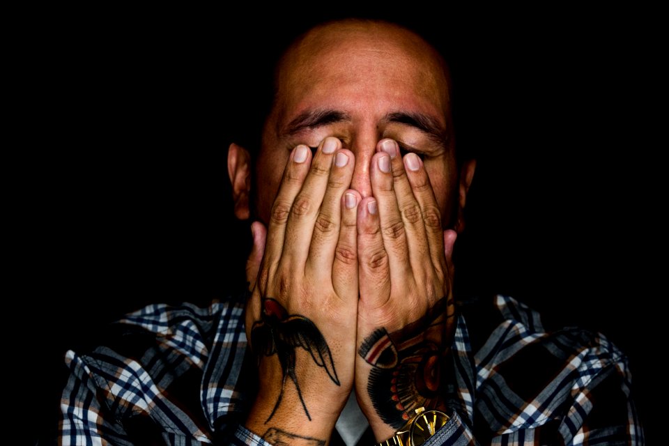 man wearing black, white, and gray plaid sport shirt covering his face