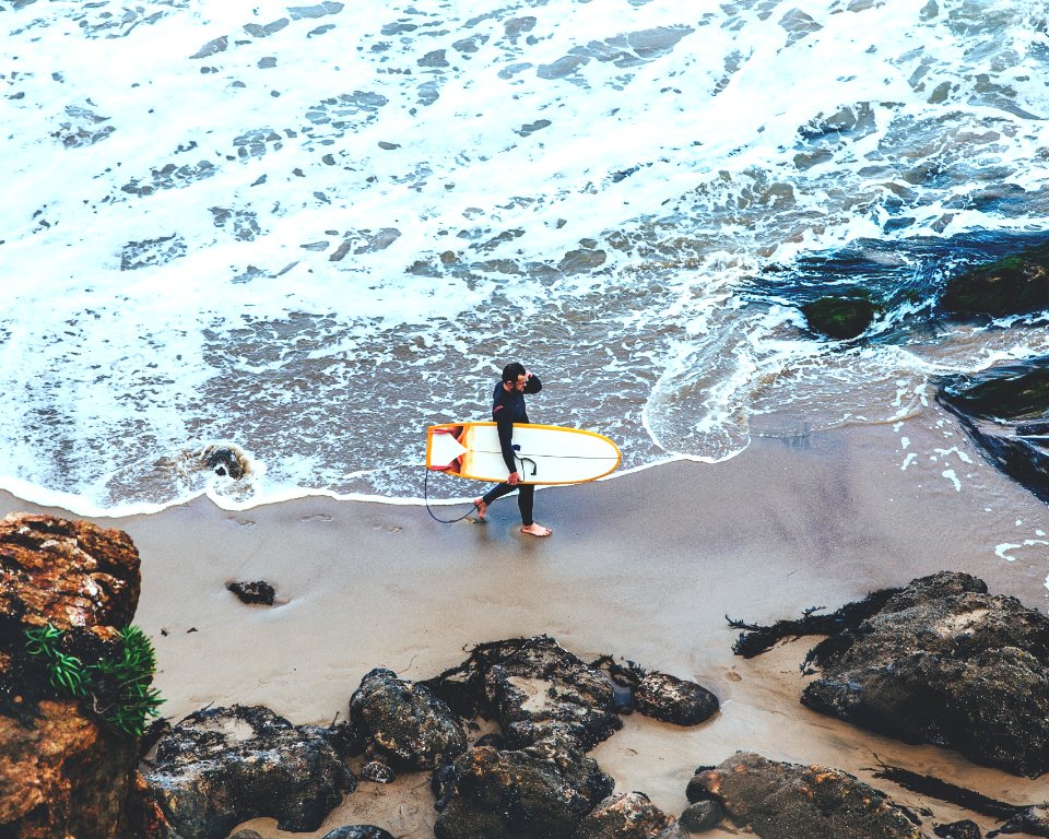 man holding surfboard walking on seashore during daytime