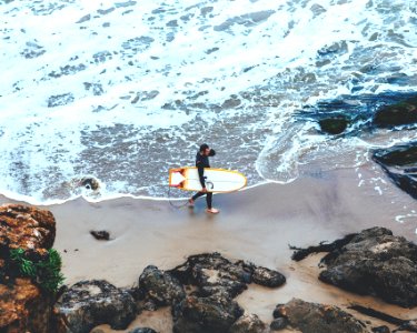 man holding surfboard walking on seashore during daytime photo