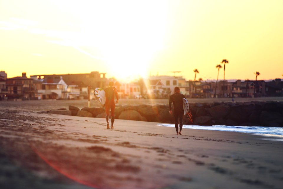 two person walking on seashore while holding surfboards