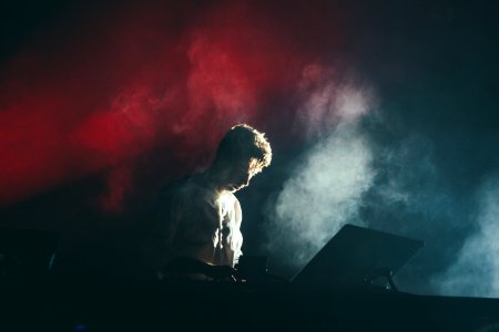 A musician in a white shirt on stage with white and red lights breaking through the smoke behind his back photo