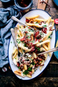bacon strips and melted cheese topped fries on oval white and blue platter with gray stainless steel forks photo