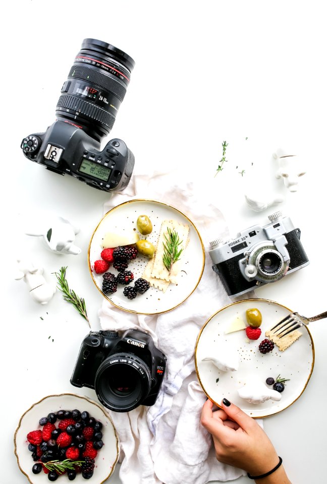 three assorted cameras near fruits and ceramic figurines