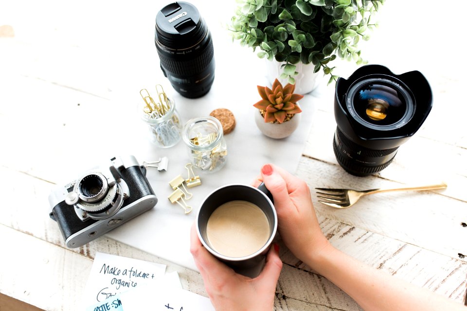 person holding black ceramic coffee mug beside black DSLR camera