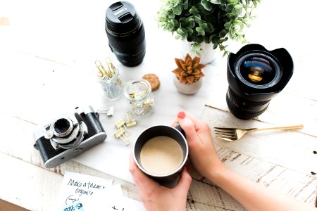 person holding black ceramic coffee mug beside black DSLR camera
