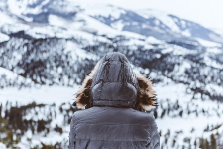 person wearing black parka hoodie in front of mountain photo