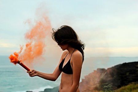 woman in black bikini holding orange smoke photo