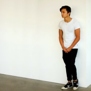man wearing white t-shirt and black jeans standing near white wall photo