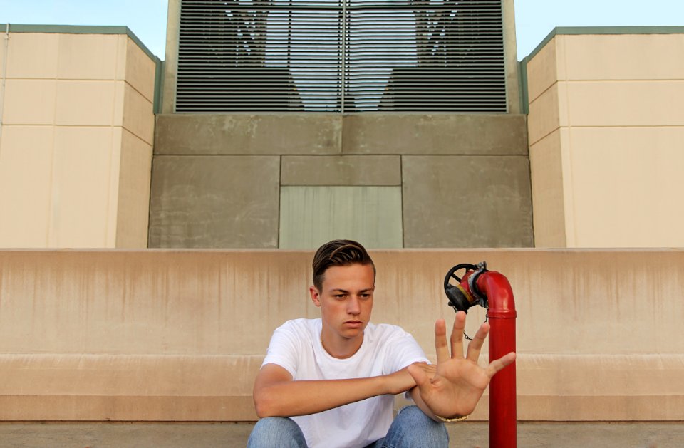man wearing white t-shirt showing left palm while sitting near building