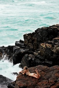 woman lying on rock formation on seashore photo