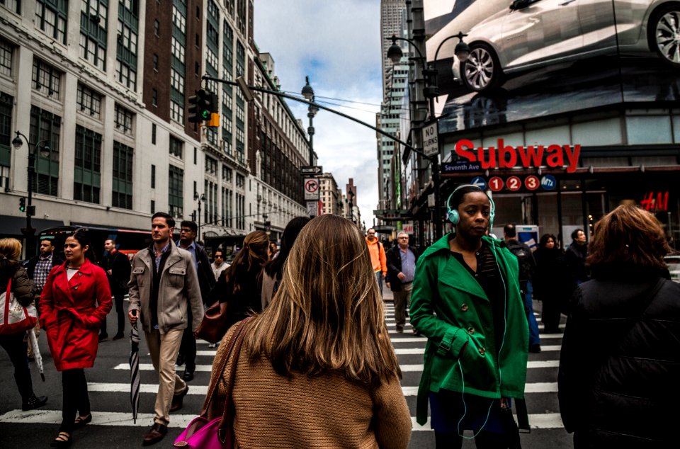 woman wearing green jacket walking on the pedestrian lane during daytime