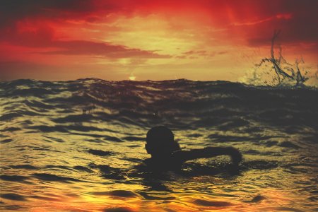 person swimming on body of water under red and orange sky photo