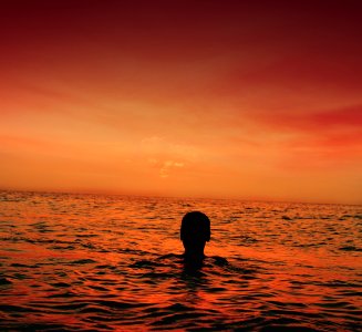 silhouette of person in ocean during sunset photo