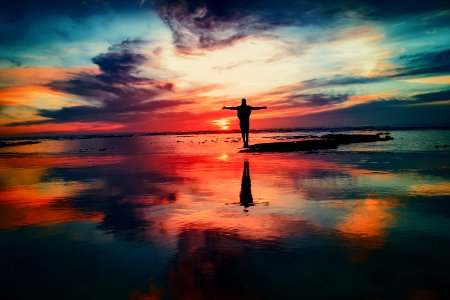 silhouette of person standing on rock surrounded by body of water photo