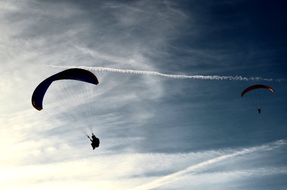 two people riding parachute on clouds during daytime