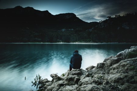 a man sits on a rock staring across a lake at dusk photo