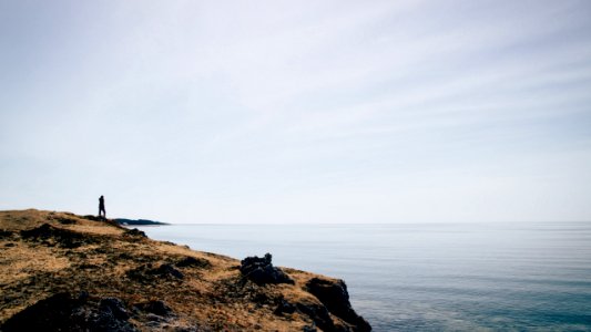 silhouette of person standing on mountain cliff near sea photo