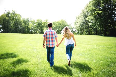 man and woman walking on green grass field surrounded with trees photo