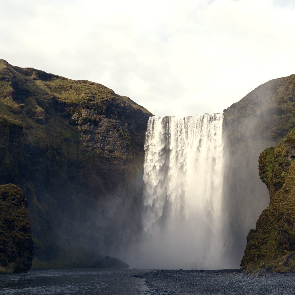 waterfalls between green mountains under cloudy sky
