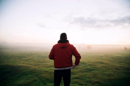 photo of man wearing red jacket facing horizon photo