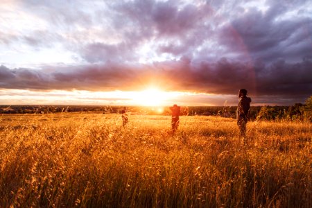 three person standing on brown grass under white clouds during sunset photo