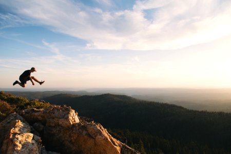 man jumping on brown rock mountain during daytime photo