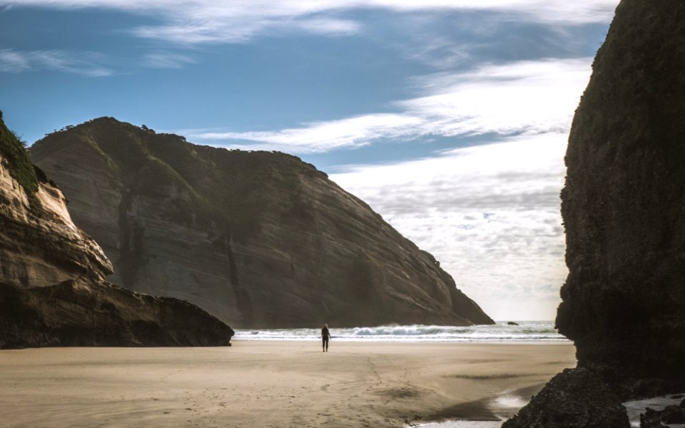 person standing on seashore between mountains
