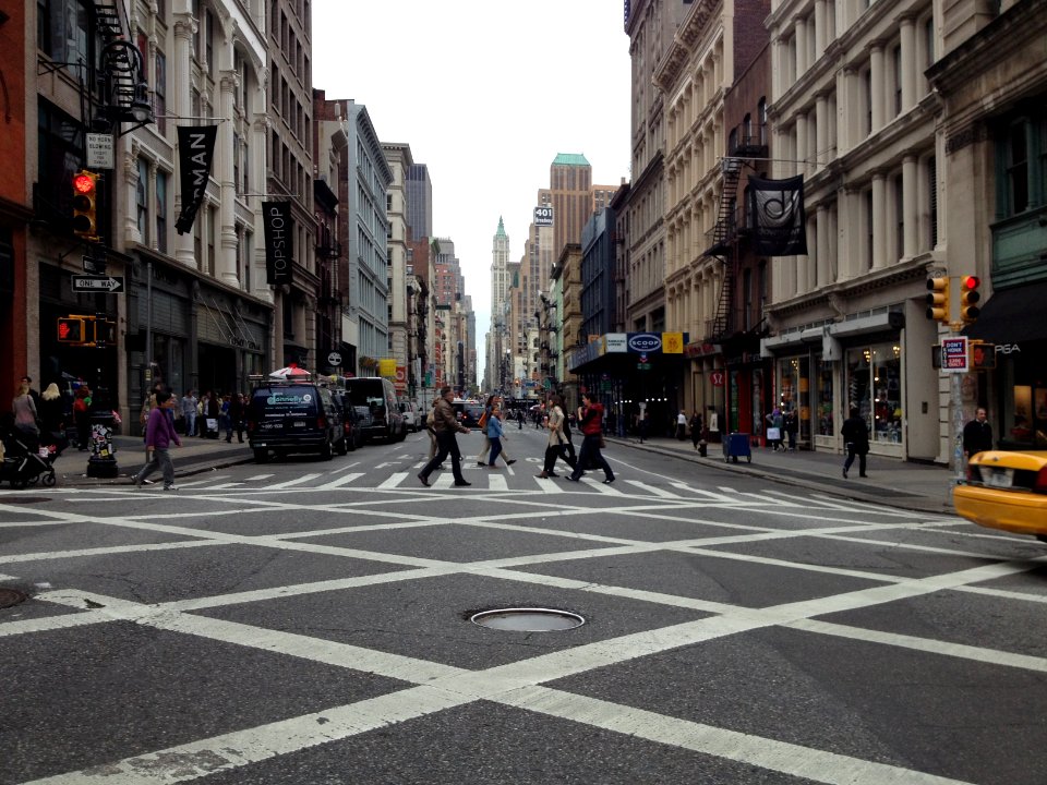 people walking on black and white concrete road between high buildings under white sky during daytime
