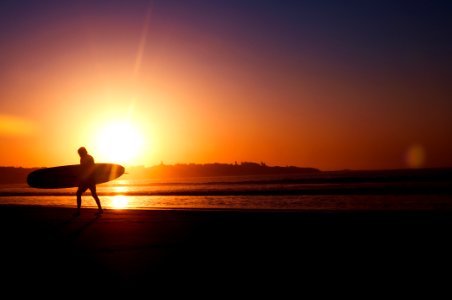 silhouette of man holding surfboard near seashore during sunset photo