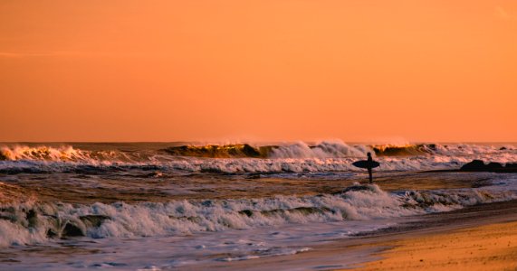 Surfer standing in shallow water, looking at waves at sunset in Bradley Beach
