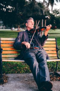 An older man playing a violin on a park bench. photo