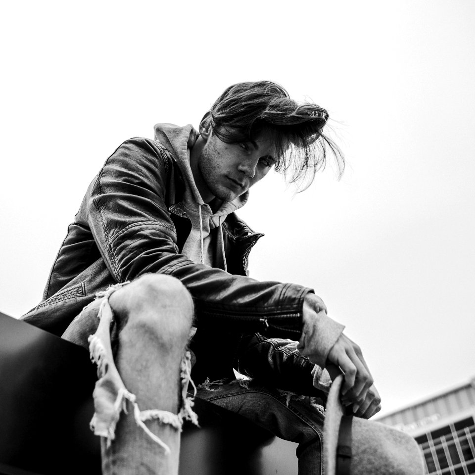 grayscale photo of man swearing leather jacket sitting on floor near building
