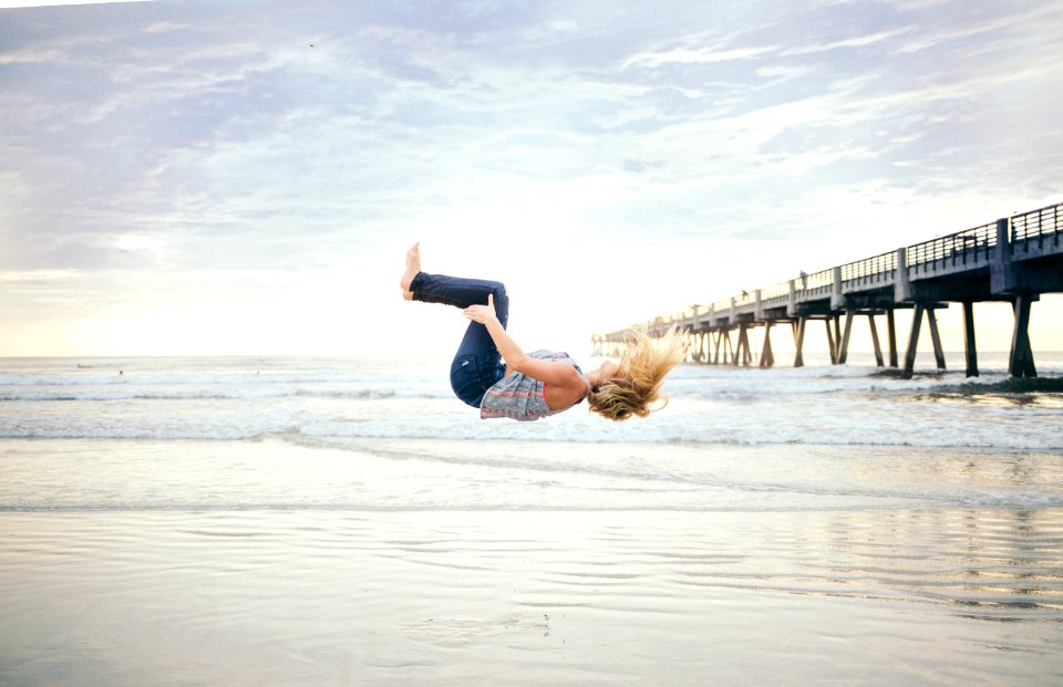 woman doing a back flip on beachshore