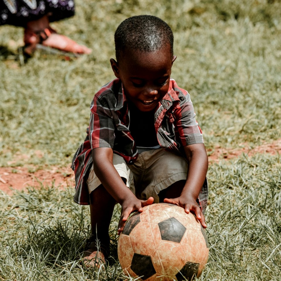 smiling boy sitting while holding soccer ball at daytime