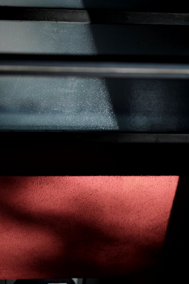 Sunlight on a black steel surface above a rough red wall