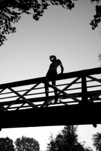 grayscale photography of man sitting on edge of bridge photo