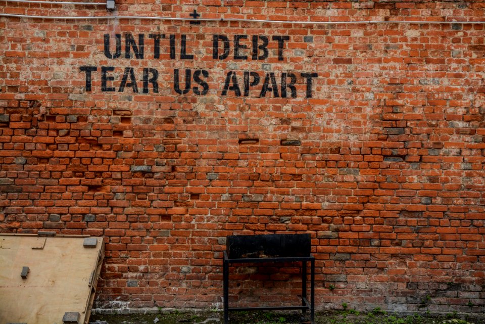 Until debt tear us apart printed red brick wall at daytime photo