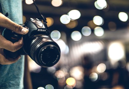 bokeh photography of person holding Nikon DSLR camera with strap photo
