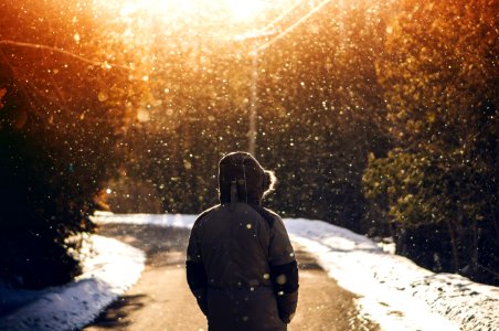 person wearing hoodie standing in middle of road with falling snow photo